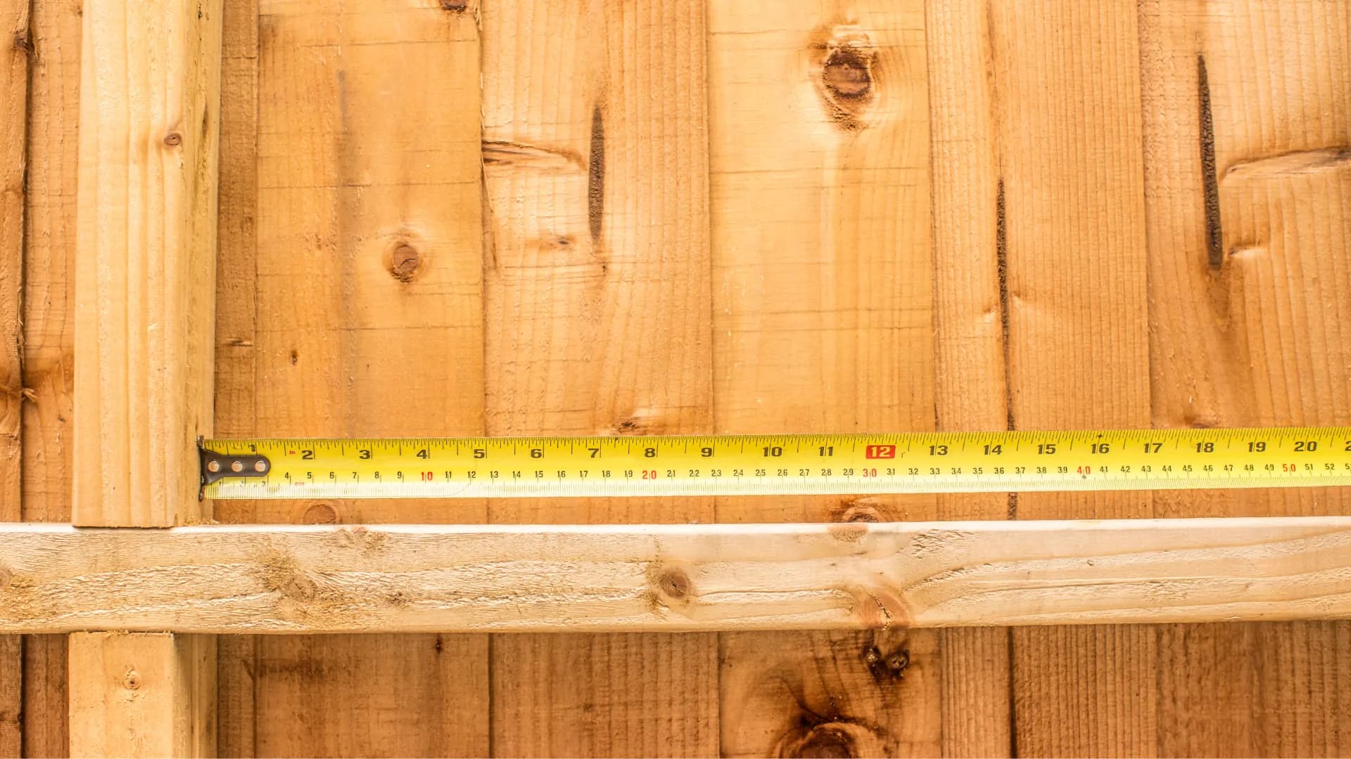 A tape measure laid along the base of a wooden fence panel before marking a hedgehog opening