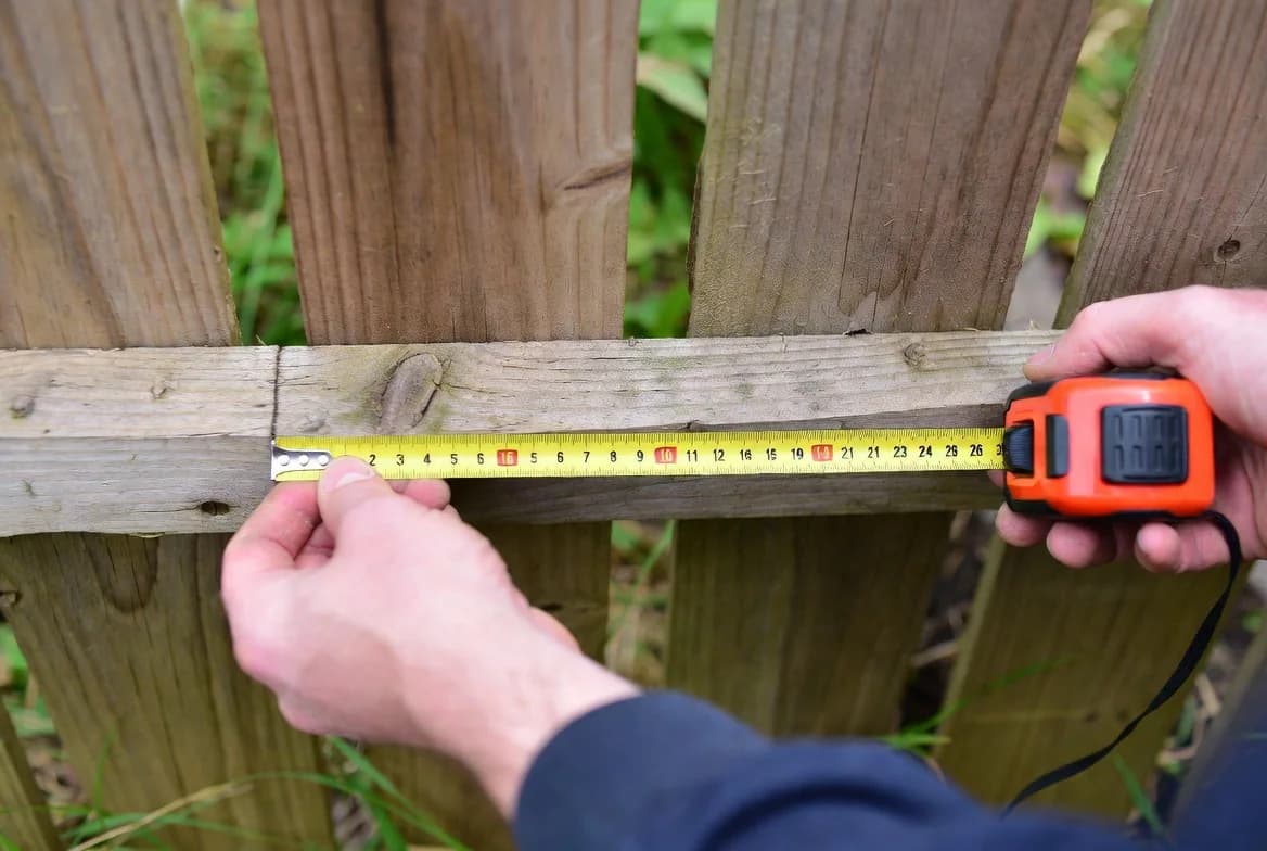 A person measuring the bottom of a wooden fence before marking a hedgehog opening
