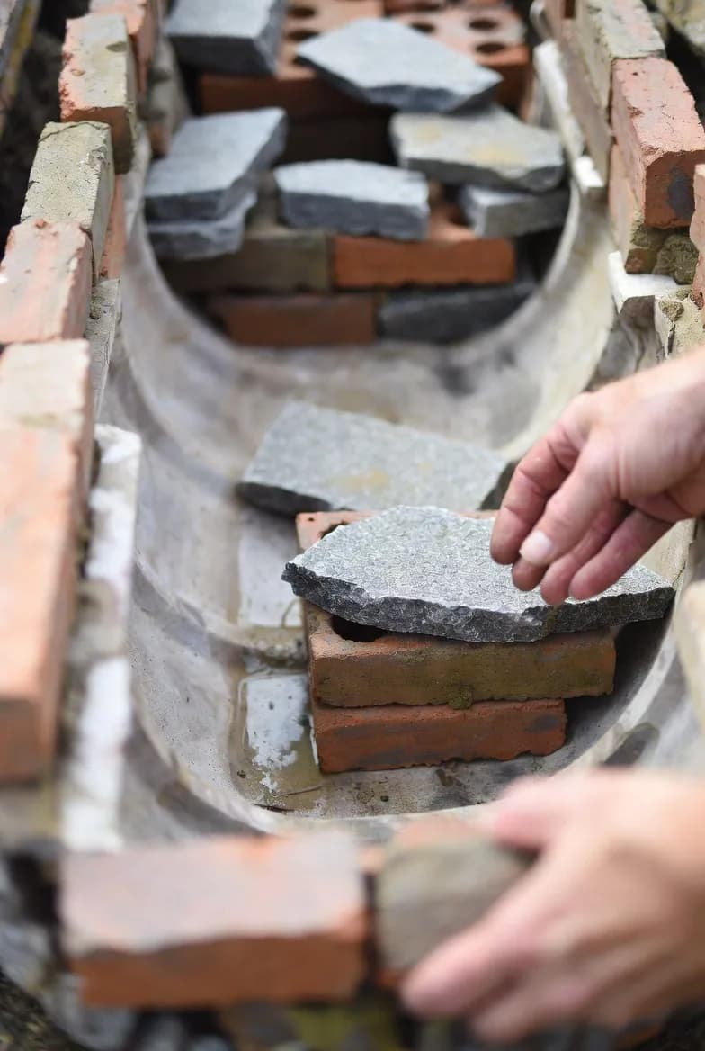 Bricks and flat stones being arranged to create different levels in a lined garden pond